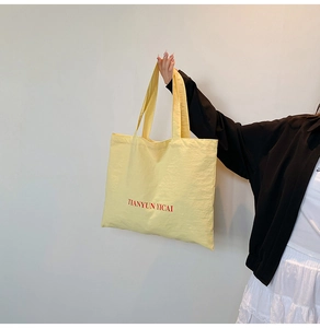 Detail of light yellow nylon tote bag featuring red TIANYUN YICAI brand text print