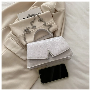 Detail of white crocodile embossed handbag featuring a silver V-shaped buckle and chain