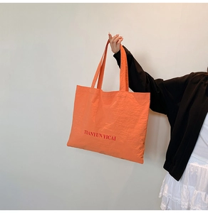 Close-up of orange nylon tote bag with text detail and long shoulder straps