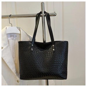 Dettaglio della borsa tote nera intrecciata con rivetti argentati su un supporto di metallo