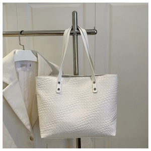 Dettaglio della borsa tote bianca intrecciata con rivetti metallici sui manici in spalla