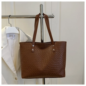 Dettaglio borsa tote marrone intrecciata con rivetti argento sui doppi manici