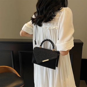 Elegant black square handbag with glitter flap and gold trim worn by a model in a stylish setting