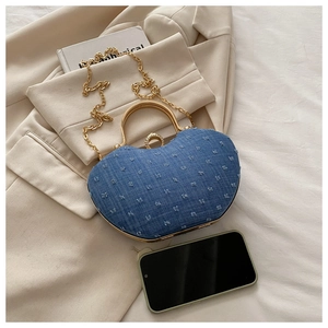 Detail of blue denim heart cloud bag with gold chain strap and crystal clasp beside phone