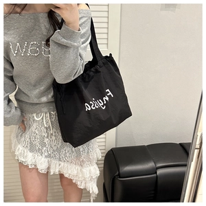 Detail of black tote bag with white typography and drawstring, shown in a mirror selfie
