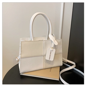 Detail of color-block white handbag featuring fixed handles and a fashion brand tag