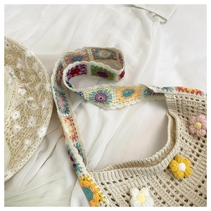 Detail of handmade crochet shoulder bag with floral 3D accents and colorful strap
