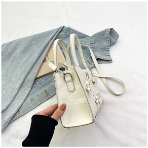 Détail du sac blanc brillant avec nœuds 3D et perles sur un tissu blanc texturé