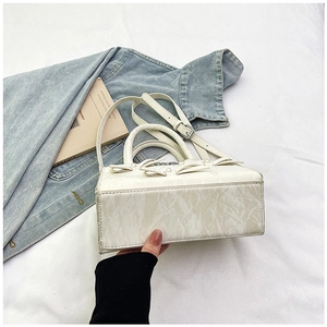 Détail d'un sac plissé blanc avec perles et nœud sur un fond de tissu doux