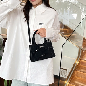 Sac cabas noir élégant avec nœuds en perles, porté par un mannequin en chemise