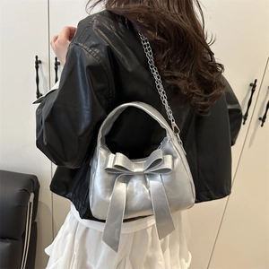 Sac à main argenté avec grand nœud et bandoulière chaîne porté par un mannequin de dos