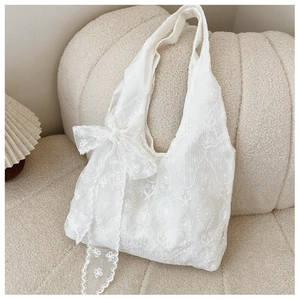 Détail d'un sac cabas en dentelle blanche avec broderie florale et grand ruban