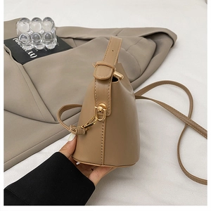 Detail of a beige leather bucket bag with fine stitching, gold hardware, and long strap