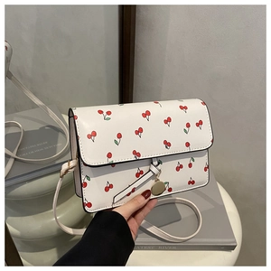 Gros plan sur le sac carré blanc avec imprimé cerise et pendentif doré métallique