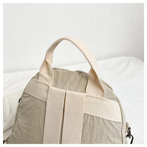 Detailed view of beige backpack handles with reinforced stitching and textured nylon fabric