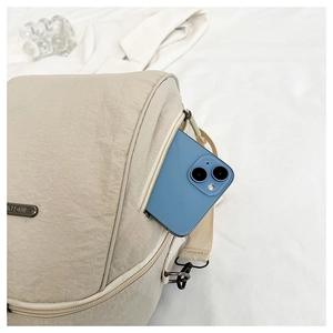 Detail view of beige nylon backpack showing side zipper pocket holding a smartphone