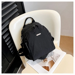 Close-up of a minimalist black nylon backpack with metal logo and front zipper detail