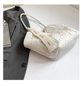 Detail of white quilted tote bag with colorful embroidery and wide canvas shoulder strap