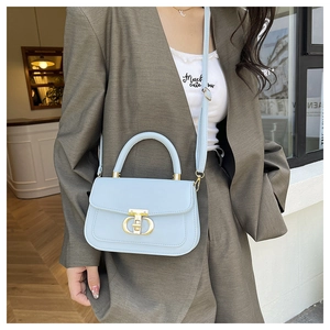 Détail du sac bandoulière bleu clair avec boucle dorée sur un blazer gris