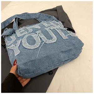 Macro detail of the frayed edge denim fabric and embroidered letters on blue tote bag
