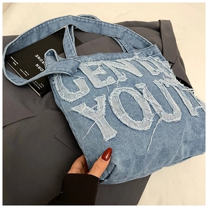 Detail of blue denim tote bag featuring white frayed letter patch and durable strap