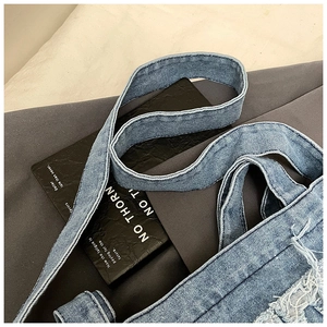 Detail of washed blue denim tote bag with frayed edges and seamless shoulder strap