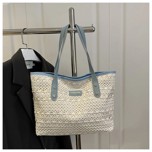Detail of blue and beige woven tote bag showing crochet texture and metallic brand logo