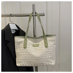 Close-up of white woven tote bag with green leather handles and brand metal plaque