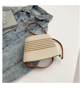 Detailed view of woven straw bag with brown stripes and adjustable faux leather strap