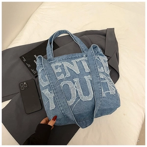 Detail of blue denim tote bag with Gentle You letter patchwork and raw fringe edges