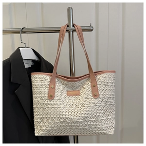 Close-up of beige woven tote bag with pink leather trim and metallic rivets detail