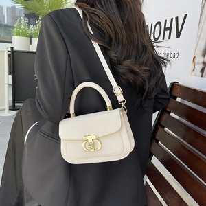 Sac bandoulière beige chic avec fermoir en T doré, porté à l'épaule dans un décor urbain