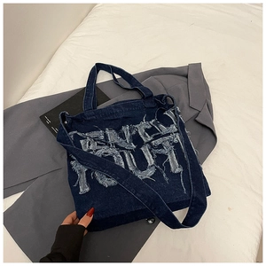 Detailed macro view of large frayed denim letter patches on the dark blue tote bag