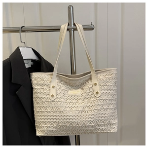Detail of hollow-out straw woven tote bag with metallic logo plate and leather straps