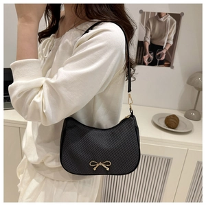 Detail of black crescent shoulder bag with golden bow and diagonal textured finish