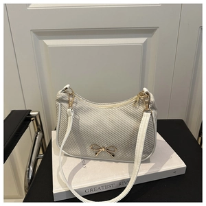 Close-up of gray woven hobo bag with golden bow hardware on white book and chair