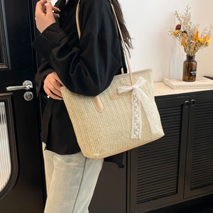 Straw tote bag with white lace bow and leather strap shown on shoulder for summer style