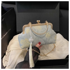 Détail de pochette florale vintage avec chaîne dorée et gland dans une boîte cadeau