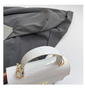 Detail of white crocodile embossed handbag featuring golden metal rings and square lock