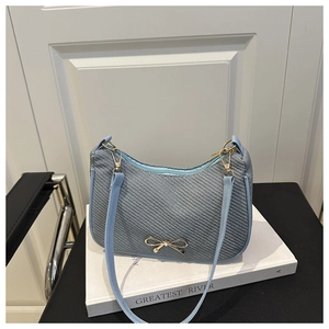Detail of light blue woven underarm bag featuring a golden bow metal clasp decoration