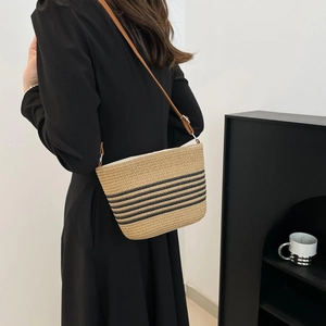 Chic woven beach crossbody bag with black stripes and brown leather strap on a model