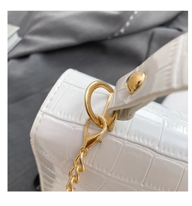 Close-up of shiny gold hardware and crocodile texture on white handbag detail