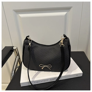 Close-up of black woven crescent bag featuring a gold metal bow and thin strap