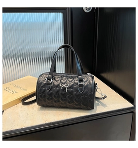 Détail du sac cylindrique noir avec matelassage en cœur et décoration de nœud argenté