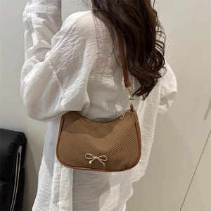 Brown woven half-moon shoulder bag with golden bow pendant and leather strap for women