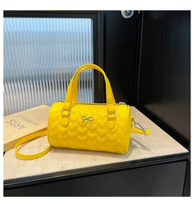 Détail du sac cylindrique jaune vif avec surpiqûres en cœur et nœud argenté