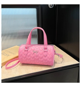 Détail du sac cylindrique rose avec matelassage cœur et nœud argenté sur surface en pierre