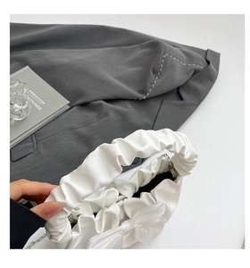 Close-up of white pleated cloud handbag with large bow detail and silver chain strap