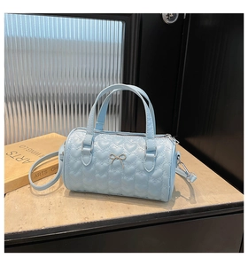 Détail du sac cylindrique bleu clair avec matelassage cœurs, nœud doré et fermeture éclair