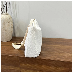 Detail of white nylon shoulder bag with crinkled texture on a dark wood surface